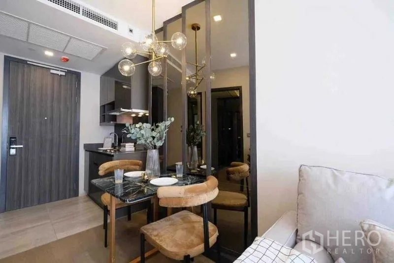 公寓 出租在Watthana, Bangkok - 大理石餐桌、吊灯与镜面装饰的用餐区，旁边是小厨房和入户门