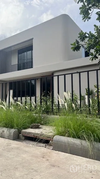 独立式住宅 出租在Lat Krabang, Bangkok - 房屋外观斜角，线条立面、黑色围栏与景观草坪。