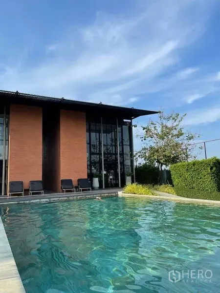 Detached House for sale in Sai Mai, Bangkok - Resort-style clubhouse with sun loungers beside an outdoor swimming pool under a blue sky.