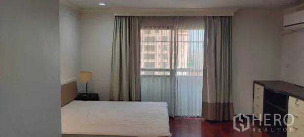 Condominium for rent in Watthana, Bangkok - Bright bedroom with large window, sheer curtains, and bedside lamp.