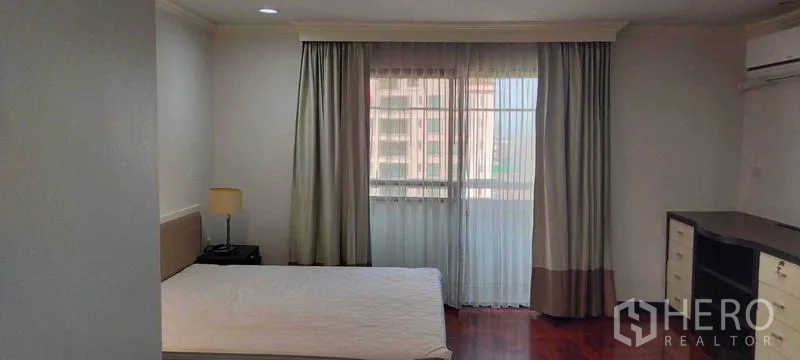 Condominium for rent in Watthana, Bangkok - Bright bedroom with large window, sheer curtains, and bedside lamp.