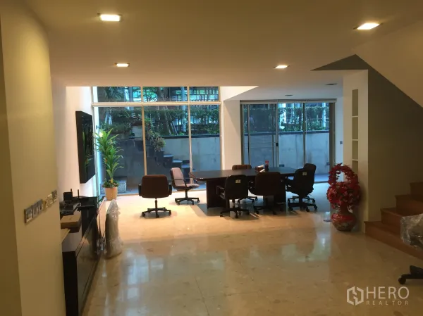 Condominium for rent or sale in Khlong Toei, Bangkok - Open-plan living and dining area with marble floors, recessed lighting and floor-to-ceiling windows overlooking greenery.