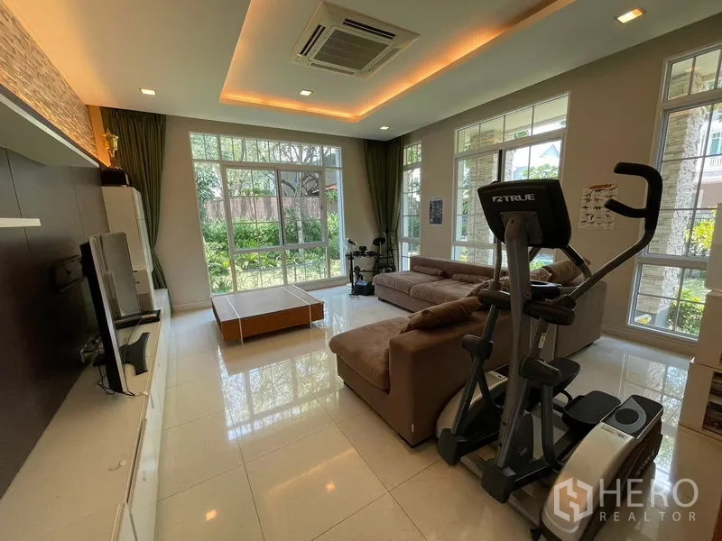 Detached House for rent in Bang Phli, Samut Prakan - Living room with L-shaped sofa, exercise equipment and garden-facing windows.