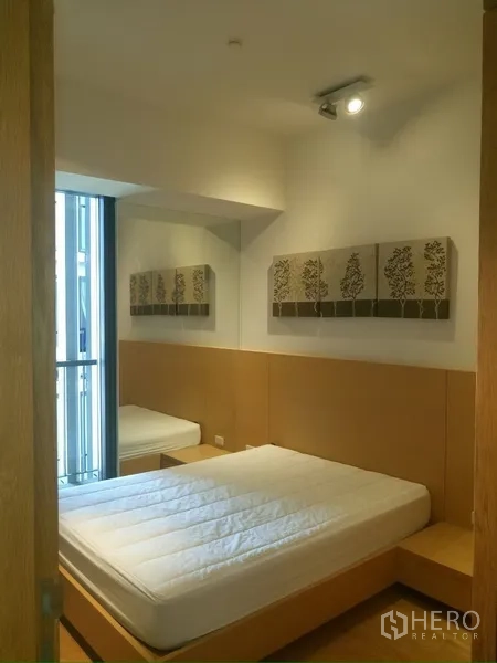 Condominium for rent in Sathon, Bangkok - Second bedroom with platform bed, wall art and access to a narrow balcony.