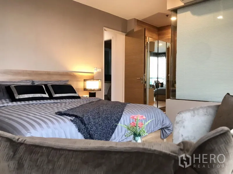 Condominium for rent in Khlong Toei, Bangkok - Primary bedroom with king bed, warm lighting and a glass-walled ensuite bathroom.