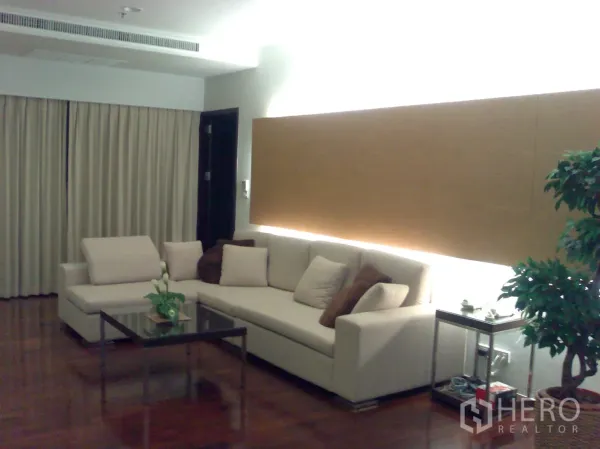 公寓 出租在Watthana, Bangkok - 现代客厅，转角沙发、玻璃茶几与暖色背景灯，木地板。