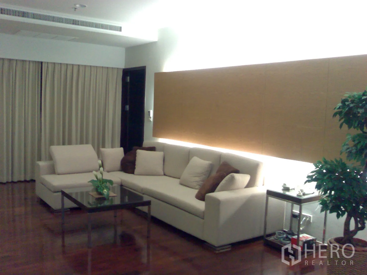 公寓 出租在Watthana, Bangkok - 现代客厅，转角沙发、玻璃茶几与暖色背景灯，木地板。