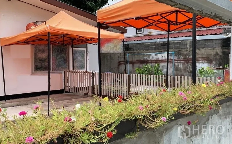Detached House for rent in Phra Khanong, Bangkok - Patio space with orange canopies and a colorful flower bed along the wall.
