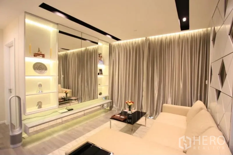 Condominium for rent or sale in Watthana, Bangkok - Living area with illuminated shelving, mirrors and beige sofa.