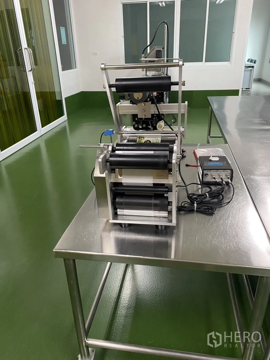 Factory for sale in Khlong Luang, Pathum Thani - Tabletop labeling unit in an open clean area with sliding glass doors.