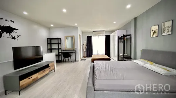 Townhouse for rent in Bang Kapi, Bangkok - Spacious master bedroom featuring a gray bed, TV console, work desk and balcony-style glass door.