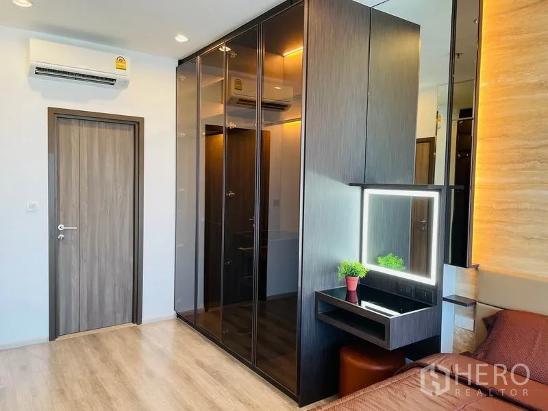 Condominium for rent in Bang Na, Bangkok - Master bedroom with glossy built-in wardrobes and an illuminated vanity.