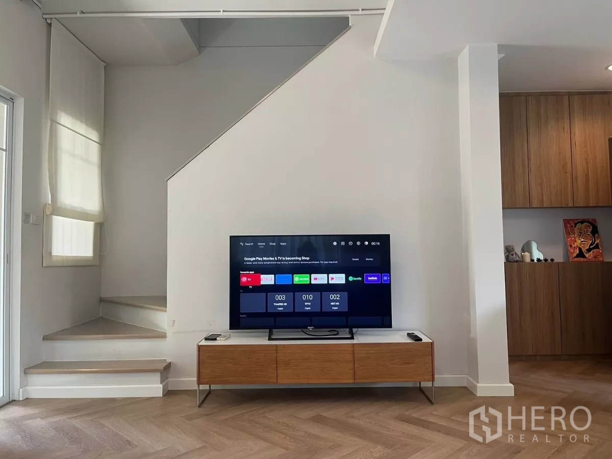 Townhouse for rent in Bang Phli, Samut Prakan - TV wall with console facing the staircase and wood cabinetry on herringbone floor.
