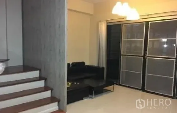 Home Office for rent in Lat Phrao, Bangkok - Bright living room with black sofa, pendant lights and sliding glass doors beside a wood staircase.