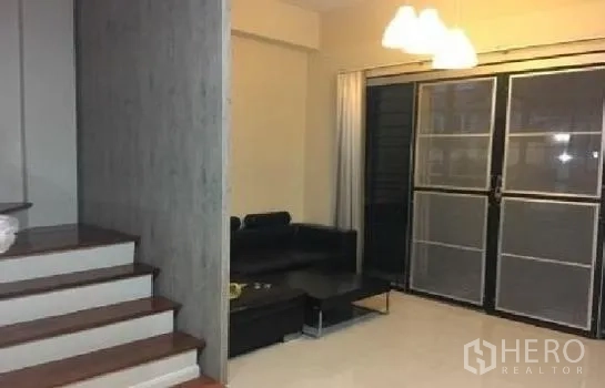 Home Office for rent in Lat Phrao, Bangkok - Bright living room with black sofa, pendant lights and sliding glass doors beside a wood staircase.