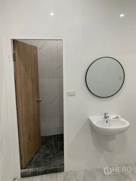 Townhouse for sale in Yan Nawa, Bangkok - Guest washroom with white sink, round mirror, and wooden door.