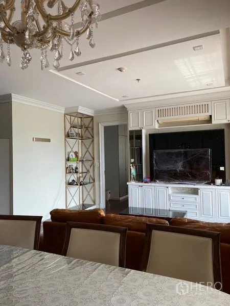 Condominium for rent in Ratchathewi, Bangkok - Elegant living room featuring white cabinetry, display shelving, and a crystal chandelier.