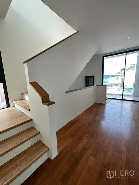 Detached House for rent in Watthana, Bangkok - Modern staircase with wooden steps leading to a bright landing and sliding doors to an outdoor balcony.