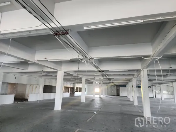 Factory for rent or sale in Khlong Toei, Bangkok - Open-plan factory floor with white concrete columns, exposed wiring and fluorescent lighting.
