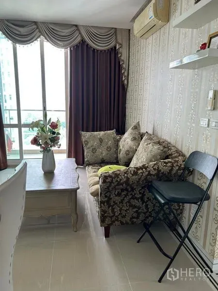 Condominium for sale in Huai Khwang, Bangkok - Compact living room with patterned sofa, coffee table and balcony door.