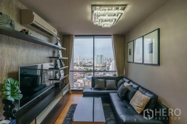 Condominium for rent or sale in Bang Rak, Bangkok - Living room with media wall, chandelier lighting, and balcony door framing downtown Bangkok.