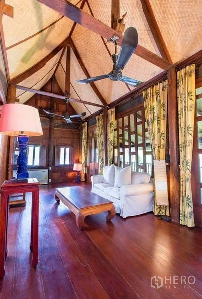Detached House for rent in Bang Na, Bangkok - High‑ceiling lounge with exposed beams, ceiling fans, wood floors and sofa.