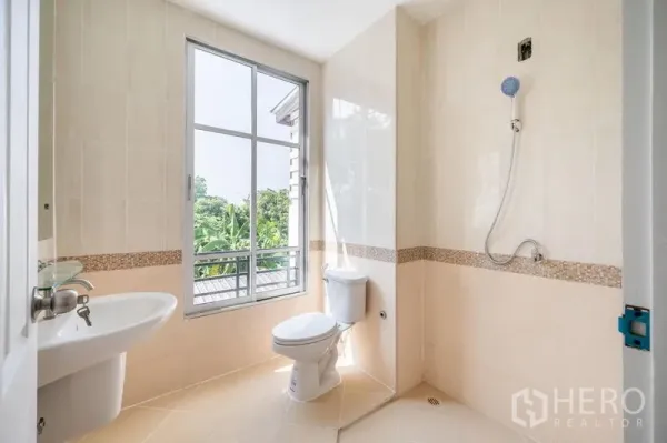 Townhouse for sale - Sunlit bathroom with large window, shower, toilet and beige wall tiles.