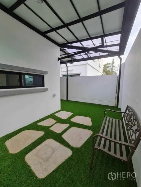 Townhouse for rent in Bang Phli, Samut Prakan - Shaded patio with bench and stepping stones on green turf beside the townhouse.
