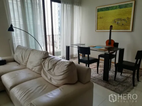 Condominium for sale in Khlong Toei, Bangkok - Living and dining area with glass-top table, sofa and balcony with city view.