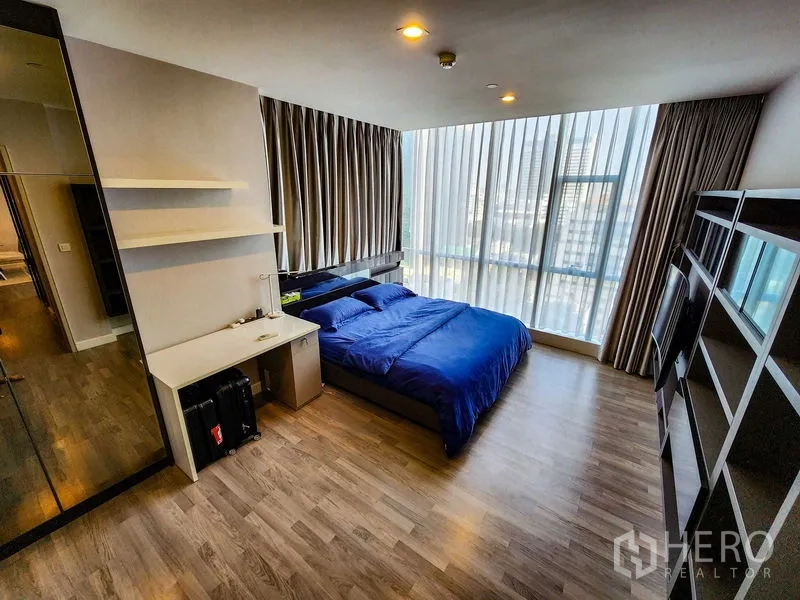 Condominium for rent or sale in Bang Rak, Bangkok - Spacious master bedroom with blue bedding and full-height windows.