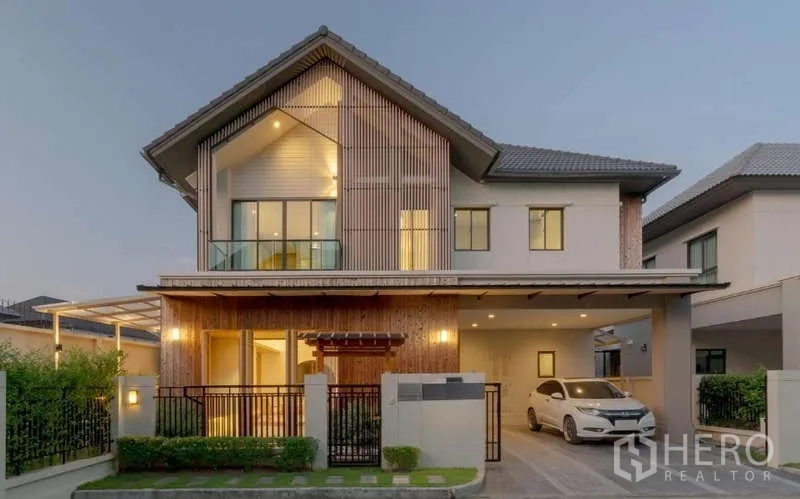 Detached House for sale in Bang Phli, Samut Prakan - Contemporary facade at dusk with gated entry, covered carport, and upper balcony.