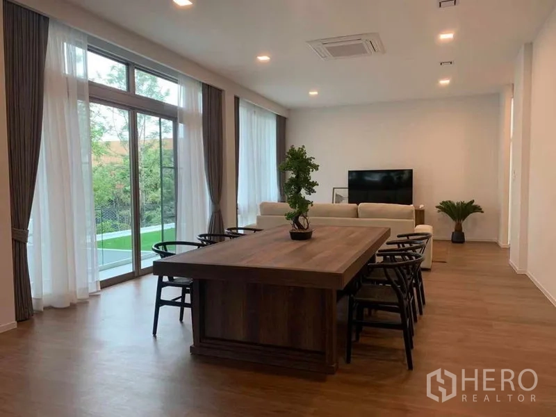 独立式住宅 出租在Saphan Sung, Bangkok - 宽敞客餐厅，木地板，落地窗与纱帘，沙发区对面为电视墙。