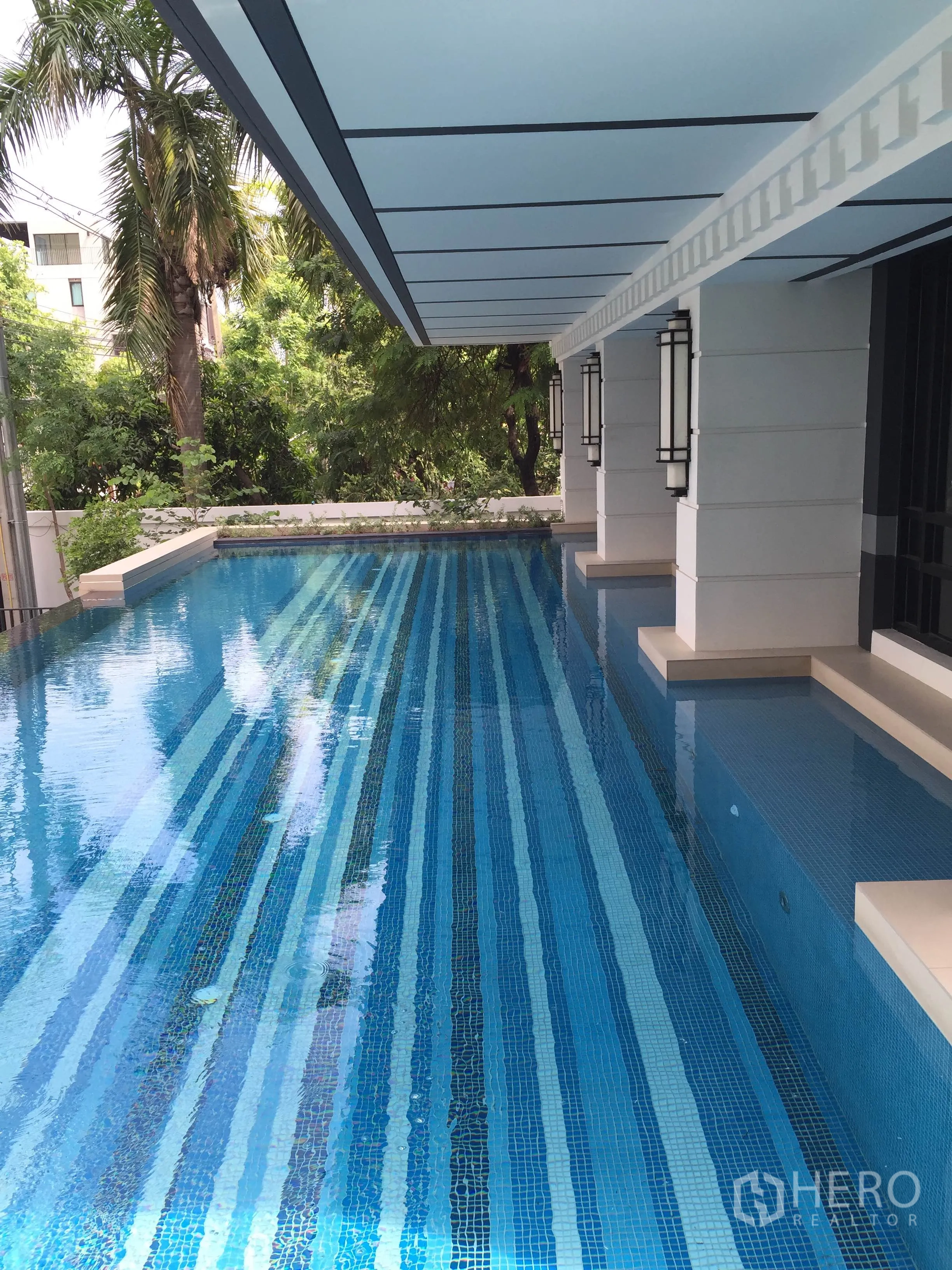 公寓 出租在Pathum Wan, Bangkok - 室外泳道池，蓝色条纹马赛克砖，带顶棚，旁有绿树。