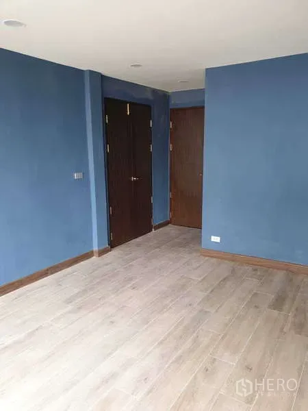 Home Office for rent in Khlong Toei, Bangkok - Freshly painted blue room with wood-look flooring and two solid doors.