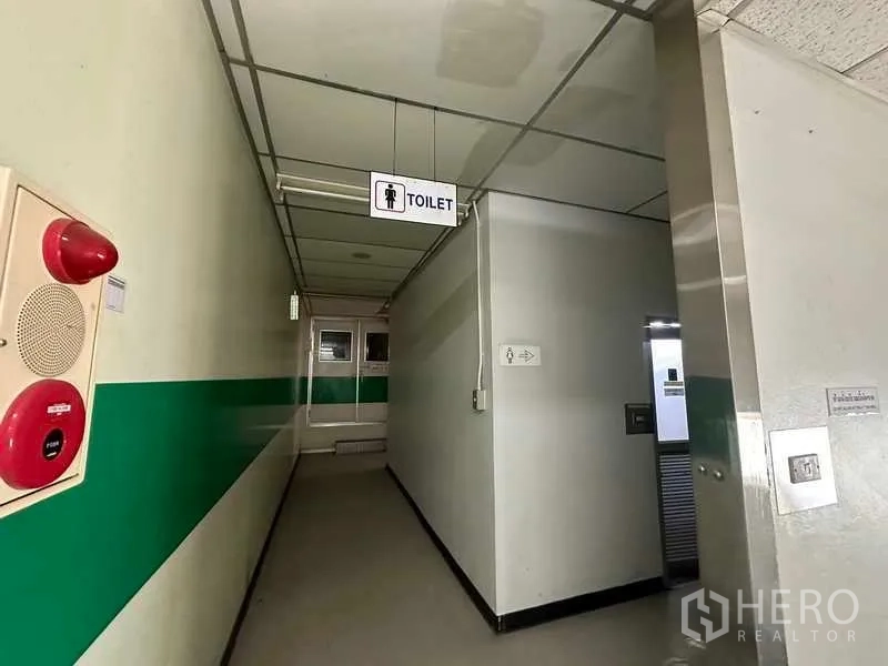 Factory for rent or sale in Thanyaburi, Pathum Thani - Internal corridor with toilet sign, green wall stripe, and fire safety equipment.
