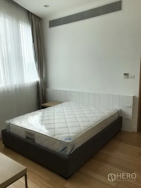 Condominium for rent in Khlong Toei, Bangkok - Cozy bedroom with new mattress, large window with sheer curtains, and wood floors.