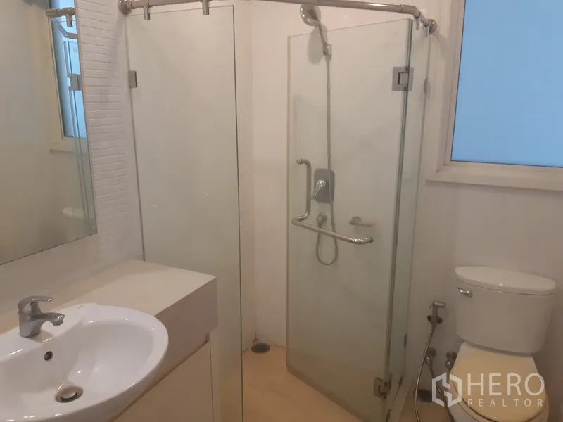Condominium for rent in Khlong Toei, Bangkok - Bathroom with glass-enclosed shower, vanity, toilet and window.