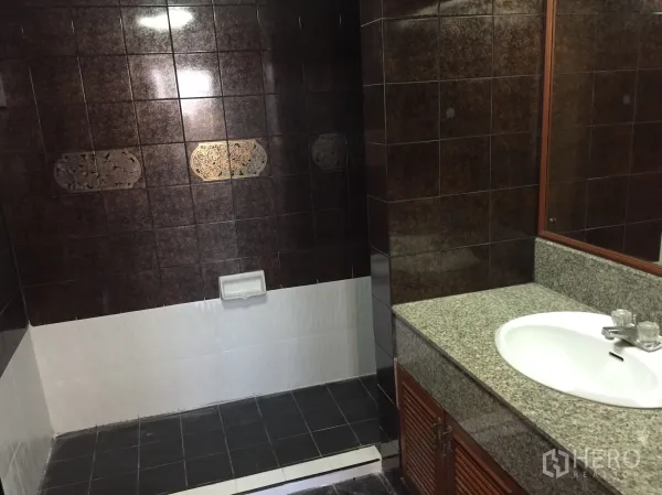 Condominium for rent in Watthana, Bangkok - Bathroom with dark tiled walls, step-in shower area, granite countertop vanity and large mirror.