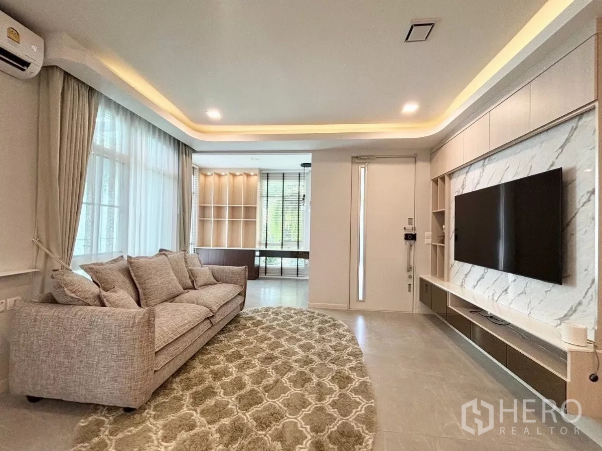 Detached House for rent or sale in Prawet, Bangkok - Bright living room in a Prawet, Bangkok detached house with large windows, a grey sofa and a marble TV wall.