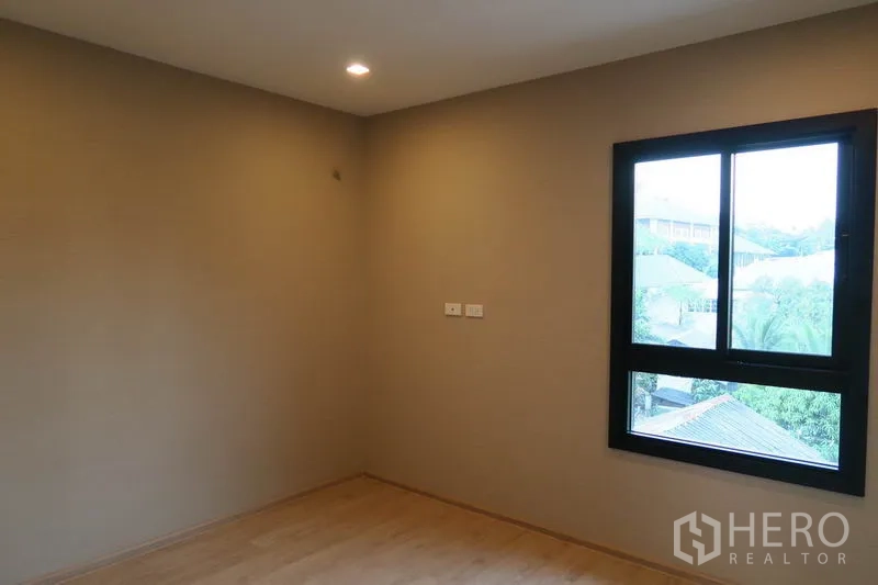 Townhouse for rent in Suan Luang, Bangkok - Cozy bedroom with recessed lights and a window framing neighborhood greenery.