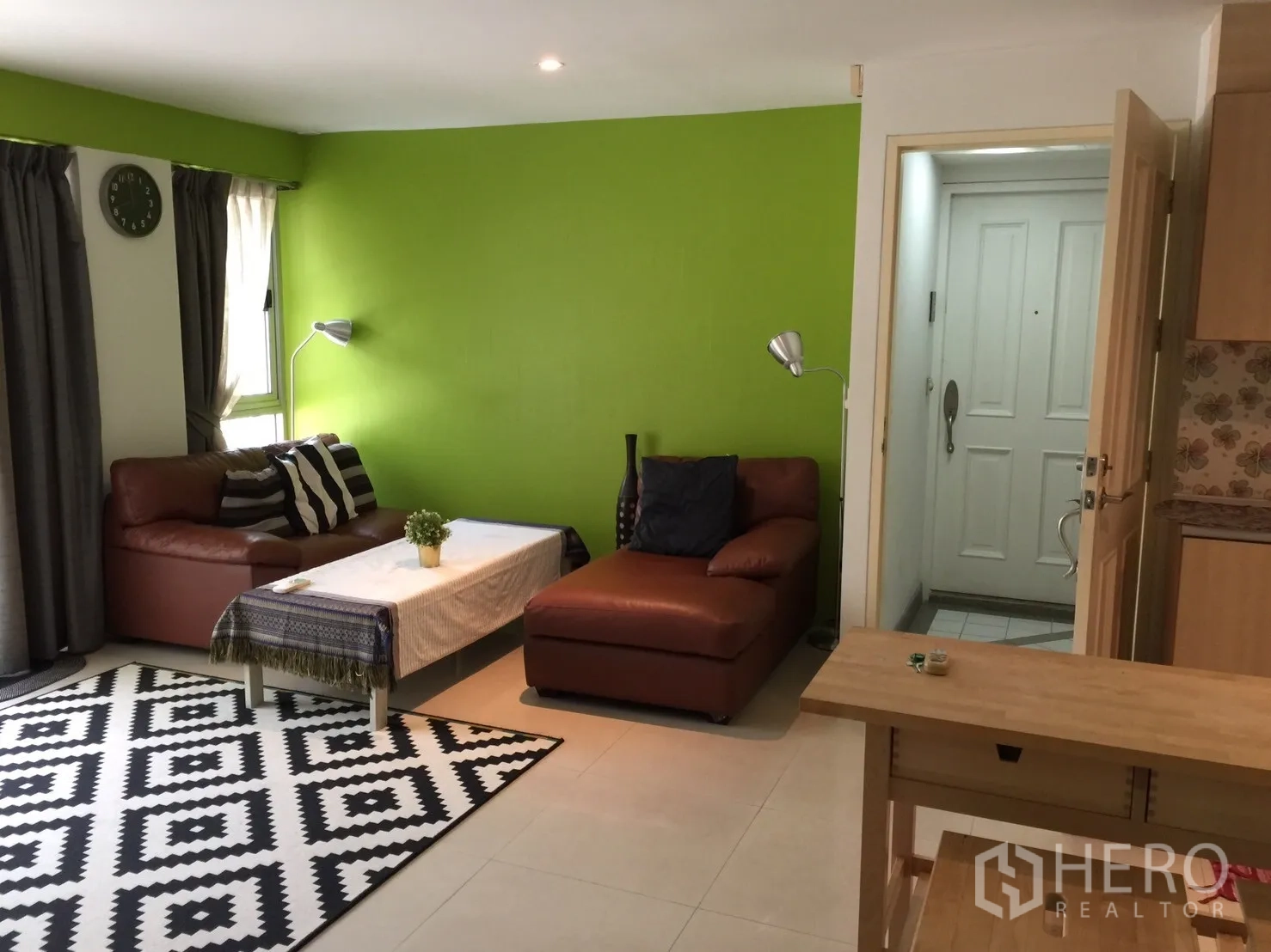 Condominium for rent in Khlong Toei, Bangkok - Bright living area with green accent wall, brown leather sofas, and the entry door.