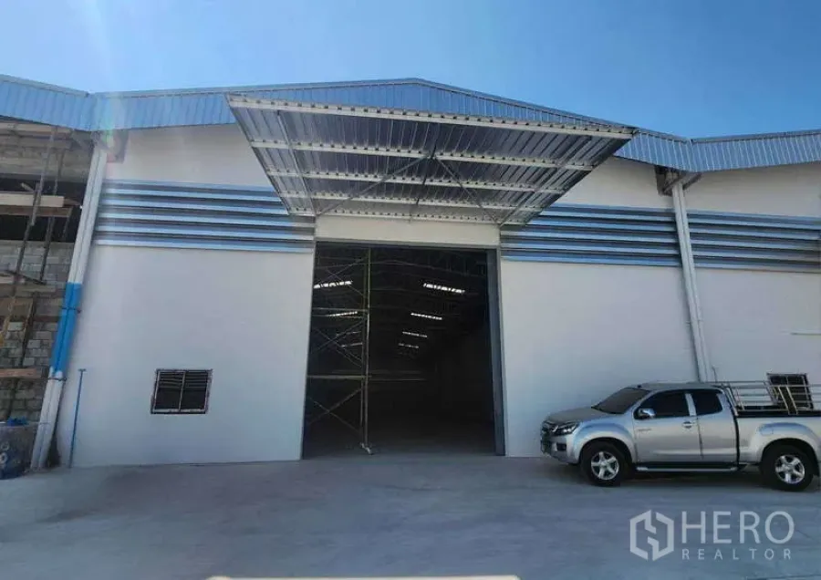 货栈 出租在Sam Phran, Nakhon Pathom - 新建仓库外观，宽大雨棚覆盖装卸区，超高入口与混凝土场地，旁停有皮卡车。