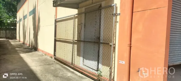Factory for rent in Khlong Luang, Pathum Thani - Side access with chain-link security gate, awning and wide concrete driveway.