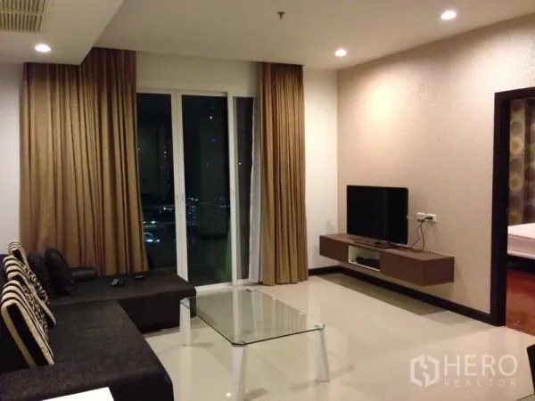 คอนโด ให้เช่าในWatthana, Bangkok - ห้องนั่งเล่นสว่าง โต๊ะกลางกระจก ชั้นวางทีวี และประตูกระจกบานเลื่อนมองเห็นวิวเมืองยามค่ำ
