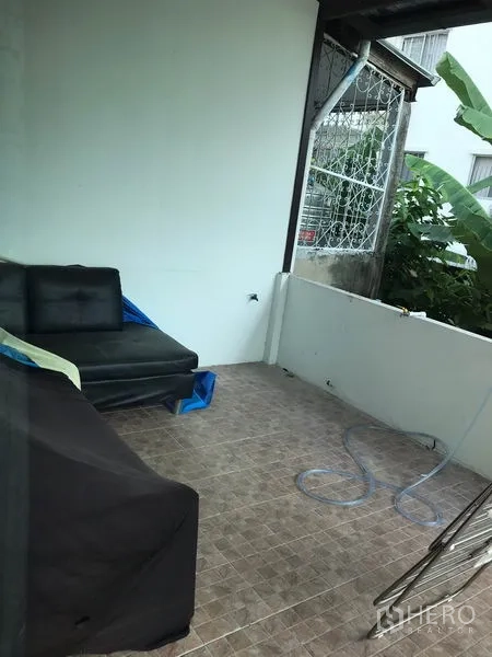 Townhouse for rent or sale in Phra Khanong, Bangkok - Covered balcony with tiled floor, low wall and seating overlooking greenery.