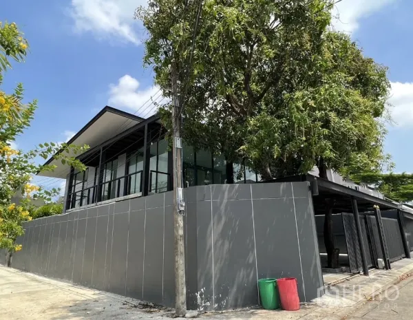 Detached House for rent or sale in Phra Khanong, Bangkok - Elevated side facade showing full-height windows above a gray boundary wall on a corner plot.