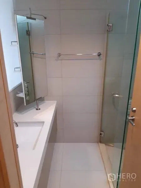 Condominium for rent in Khlong Toei, Bangkok - Clean bathroom with white vanity, mirror and a glass‑enclosed shower.