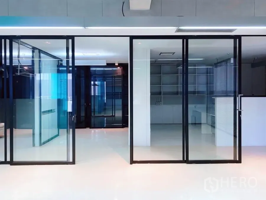 办公空间 出租在Phaya Thai, Bangkok - 一排黑框滑动玻璃门，分隔会议室与工作区的极简办公室。