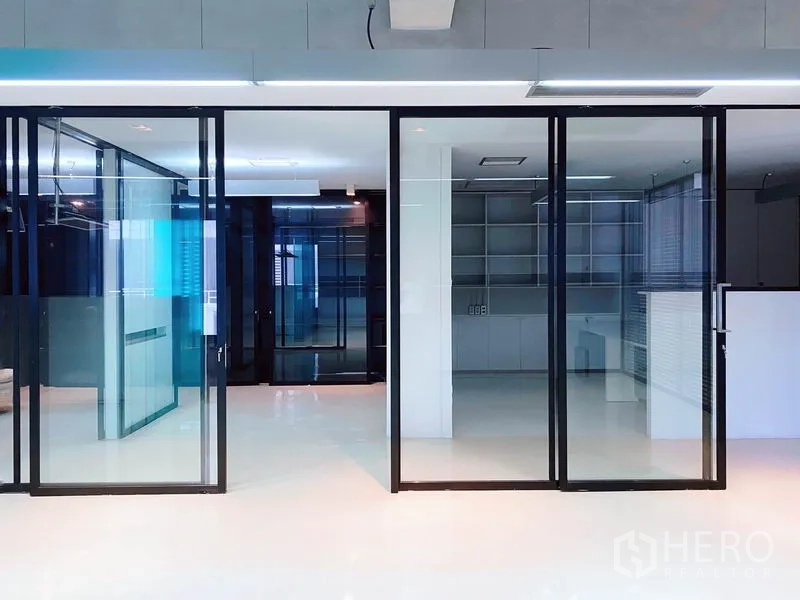 办公空间 出租在Phaya Thai, Bangkok - 一排黑框滑动玻璃门，分隔会议室与工作区的极简办公室。