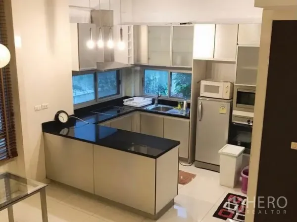 Townhouse for rent in Wang Thonglang, Bangkok - Modern U-shaped kitchen with black stone countertops, stainless appliances and windows.
